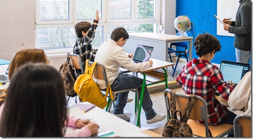 Elementary school students raising hand and learning geography in classroom