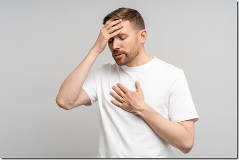 Unwell man covered forehead hand touches in region of heart feel bad suffering fever, isolated wall